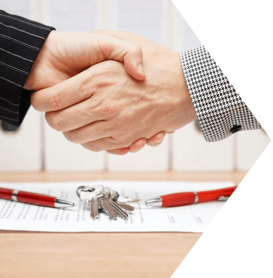 Two people shaking hands over a table with keys.